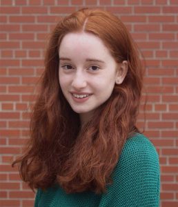 A young woman with red hair in a green sweater. Fellow Shulie Smolyanitsky.