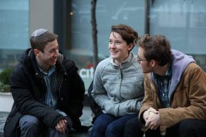 Three Bronfman Fellows sit on a bench in a city, dressed in winter clothes. They are smiling and in the middle of a deep discussion.