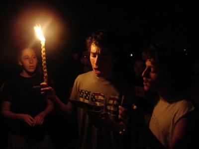 A male Fellow holds a lighted candle for Shabbat and prays with two other Fellows.