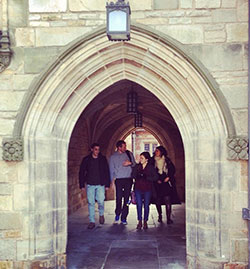 Four young people walk under a stone archway.