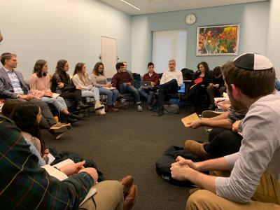 Fellows sit in a circle in a room and look at an educator, who is talking to them