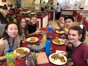 Six Fellows sitting at a table having a meal together, smiling at the camera.