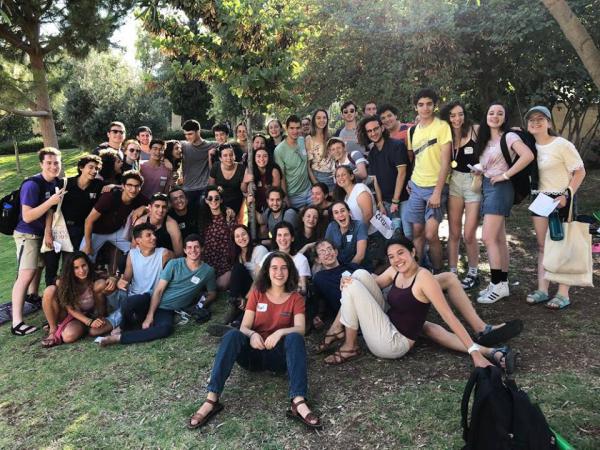 Over 40 Fellows - North American and Israeli - smile for a group photo. They are on a lawn under some trees.