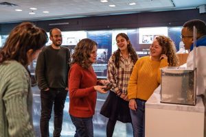 Some Fellows stand around an educator by a museum exhibit, smiling and laughing.